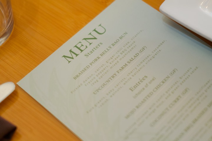 Restaurant menu on a table with a glass and napkin. Entrees and starters listed.
