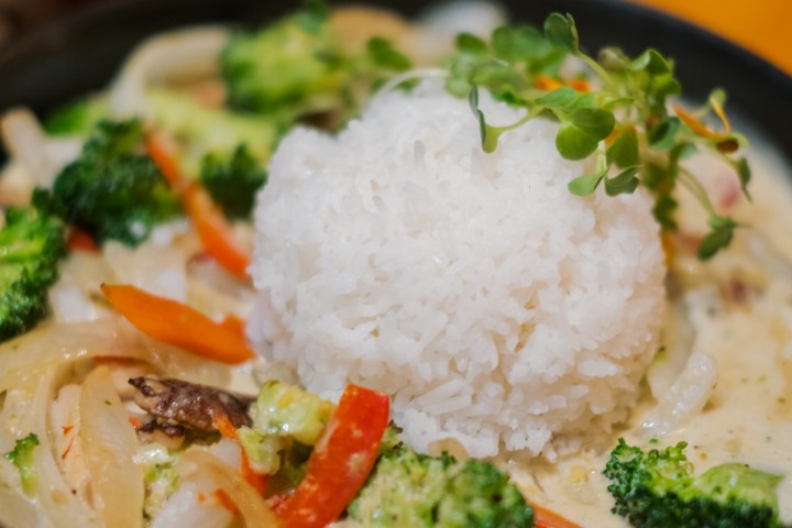 A bowl of rice with creamy vegetables, including broccoli and peppers, garnished with herbs.