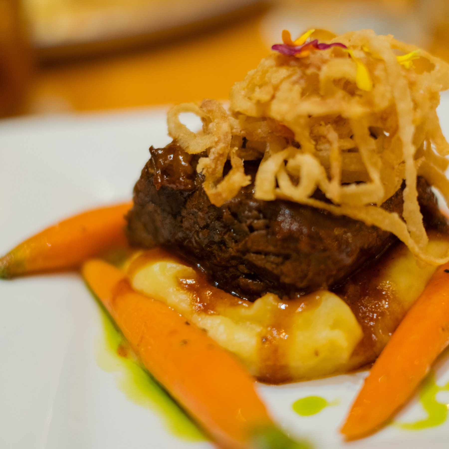 Gourmet dish with beef, mashed potatoes, carrots, and fried onion rings.