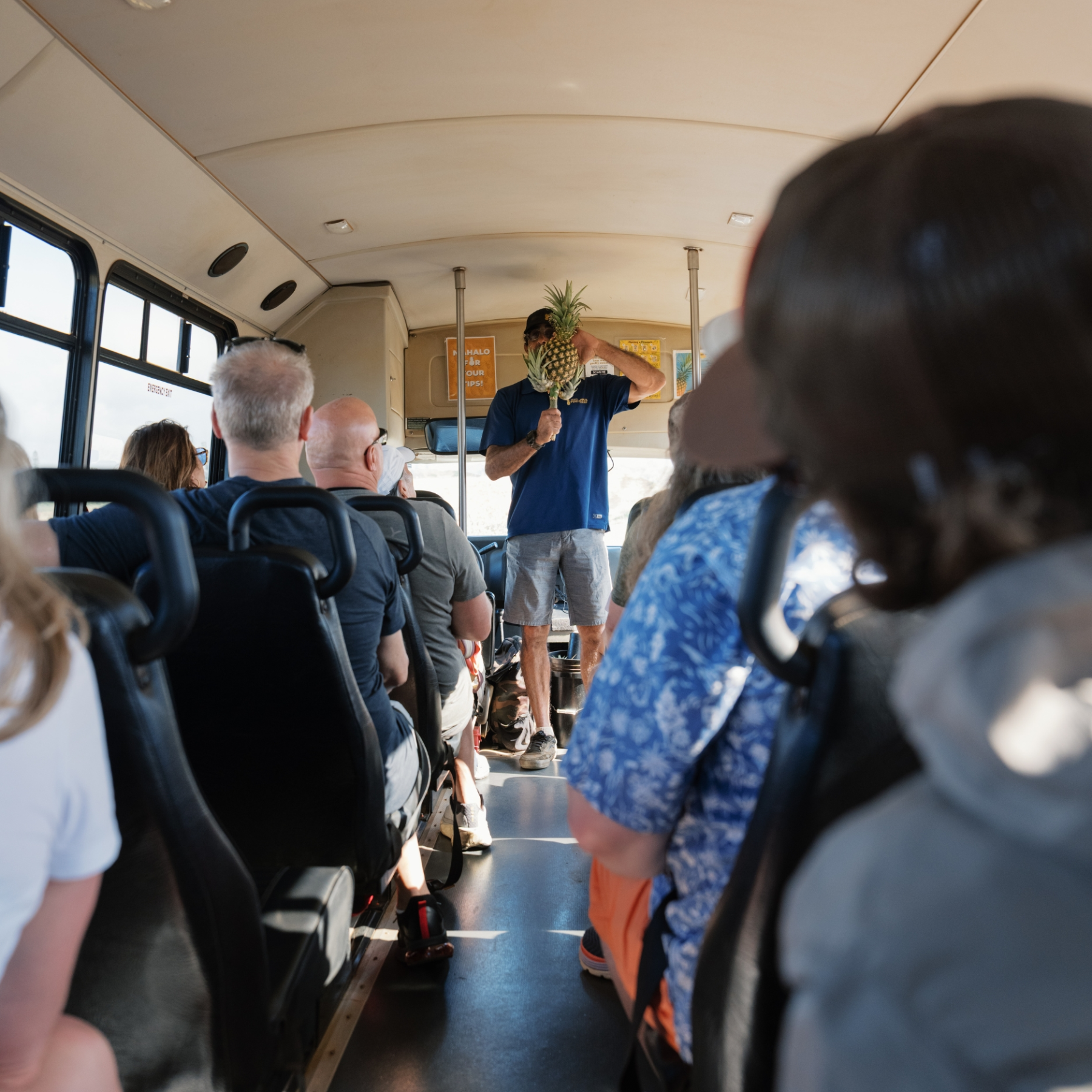 Person in blue shirt holding pineapple while speaking to bus passengers.